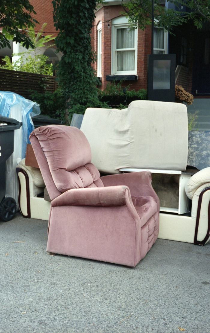 A worn armchair and sofa set out for collection outside a terraced house